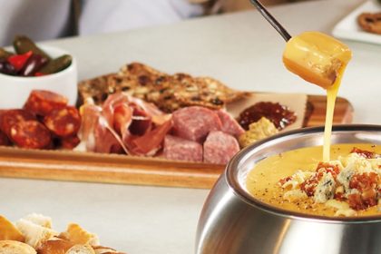 A table with cheese fondue and a selection of charcuterie meats and cheeses and pretzels