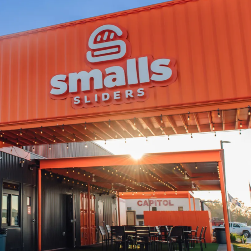 The exterior of a smalls sliders restaurant built with an orange shipping container and a burger logo on the front